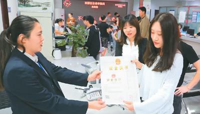 河北省承德市網(wǎng)絡(luò)代購(gòu)經(jīng)營(yíng)者陳晨(右)從工作人員手中接過帶有統(tǒng)一社會(huì)信用代碼的營(yíng)業(yè)執(zhí)照。 劉環(huán)宇攝(人民圖片)